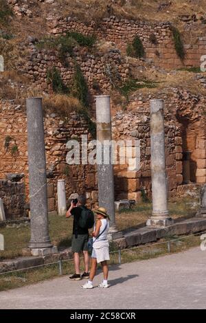 Grecia, Delfi, Sito Archeologico Greco Antico - resti del Tempio di Apollo. Sito patrimonio dell'umanità dell'UNESCO. Coppia turistica che visita il sito. Foto Stock
