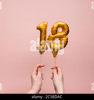 Mano femminile che tiene un numero 18 compleanno anniversario celebrazione palloncino oro Foto Stock