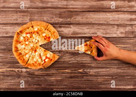 Vista dall'alto su tagliata a fette grande pizza delisiosa a quattro formaggi e mano dell'uomo che prende una fetta, su sfondo di legno o tavolo con copyspace per il testo. PROM Foto Stock