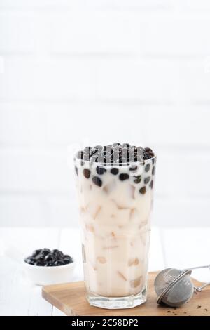 Tè al latte con tatuetta di tapioca, famosa bevanda taiwanese su sfondo bianco di legno in vetro da bere, primo piano, spazio per le copie Foto Stock