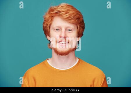 Ritratto di giovane ragazzo sorridente rosso con la testa piena di capelli che si posano su sfondo blu Foto Stock