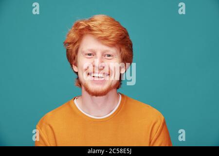 Ritratto di giovane uomo allegro con la testa piena di capelli che sorride alla macchina fotografica su sfondo blu Foto Stock