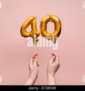 Mano femminile che tiene un numero 40 compleanno anniversario celebrazione palloncino oro Foto Stock