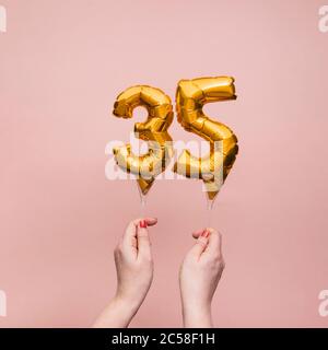 Mano femminile che tiene un numero 35 compleanno anniversario celebrazione palloncino oro Foto Stock