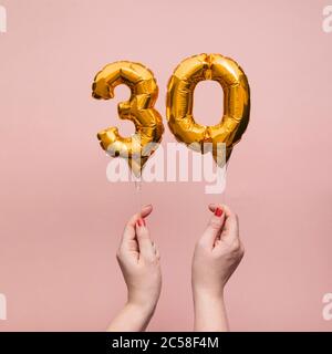 Mano femminile che tiene un numero 30 compleanno anniversario celebrazione palloncino oro Foto Stock