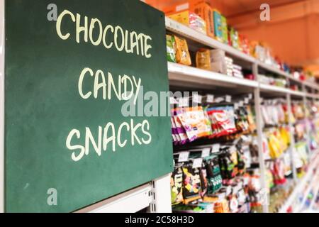 Cartello con la dicitura cioccolato, caramelle, snack alla navata del supermercato con articoli defocati sullo scaffale Foto Stock