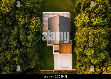 Vista aerea di casa moderna con giardino circondato da foresta durante il tramonto Foto Stock