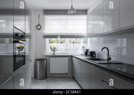 Cucina stretta con finestra e mobili moderni e grigi Foto Stock