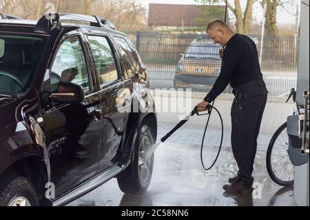 Un uomo lava un'auto in un autolavaggio senza contatto, un uomo lava un'auto marrone, Kaliningrad, Russia, 1 marzo 2020 Foto Stock