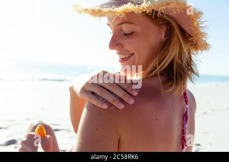 Donna che applica la crema solare sulla schiena alla spiaggia Foto Stock