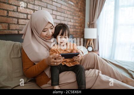 insieme la bambina e la madre guardarono lo schermo di uno smartphone mentre si sedevano sul letto Foto Stock