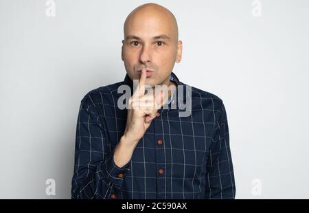 l'uomo calvo di 40 anni sta tenendo il dito indice sulle labbra chiedendo il silenzio Foto Stock