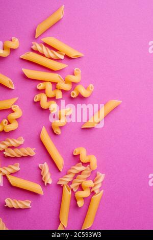 Varietà sparsa di pasta di grano dorato crudo su sfondo rosa minimale, vista dall'alto Foto Stock