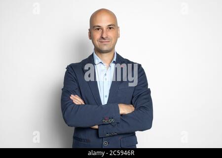 Allegro uomo baldastro di mezza età che tiene le braccia incrociate e guardando la macchina fotografica con sorriso mentre si trova in piedi sfondo grigio Foto Stock