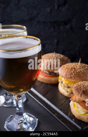 primo piano, bicchieri da birra con birra artigianale scura e chiara con schiuma, sullo sfondo di hamburger, con una varietà di ingredienti, tra cui lo shyomga Foto Stock