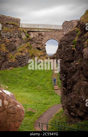 Il Castello di Dunluce circondato dal mare, dalle rocce e dalle giornate nuvolose con la pioggia sul suo cammino. Foto Stock