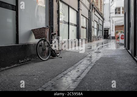 Bicicletta in stile antico con un cesto di vimini visto poggiato su una finestra di vetro per un vecchio edificio in una strada vuota della città. Foto Stock