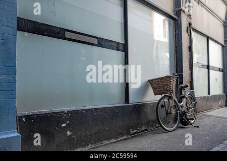 Bicicletta in stile antico con un cesto di vimini visto poggiato su una finestra di vetro per un vecchio edificio in una strada vuota della città. Foto Stock