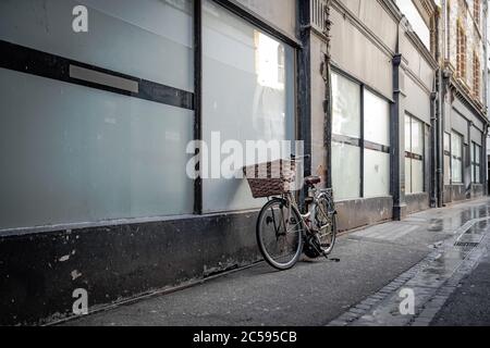 Bicicletta in stile antico con un cesto di vimini visto poggiato su una finestra di vetro per un vecchio edificio in una strada vuota della città. Foto Stock