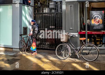 Uomo visto aspettare vicino a un caffè in un centro città occupato. Visto che teneva una borsa colorata e indossava sneaker colorate vicino a un vicolo. Foto Stock