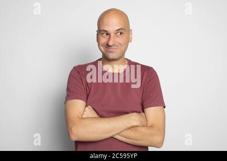 L'uomo allegro e calvo si sta guardando via con un sorriso ingannevole sul viso. Isolato su sfondo grigio studio Foto Stock