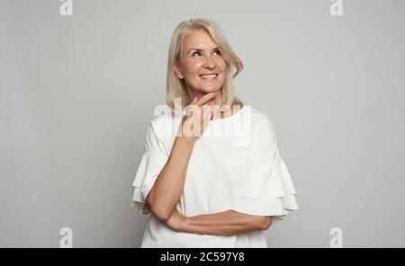 ritratto di una bella donna sorride, guardando in alto. 50 anni donna isolato sopra parete grigia studio Foto Stock