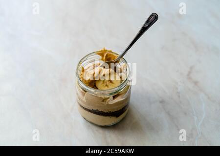 Torta di burro di arachidi cremosa Dessert con fetta di banana e torta al cioccolato in vaso / tazza di dieta Paleo. Cibo sano e biologico fatto in casa. Foto Stock