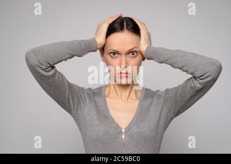 Donna scioccata tiene la testa nelle mani. Isolato su grigio Foto Stock