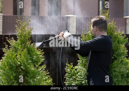 L'uomo lava il recinto di casa di campagna lavavalunotto ad alta pressione concetto di pulizia della molla Foto Stock