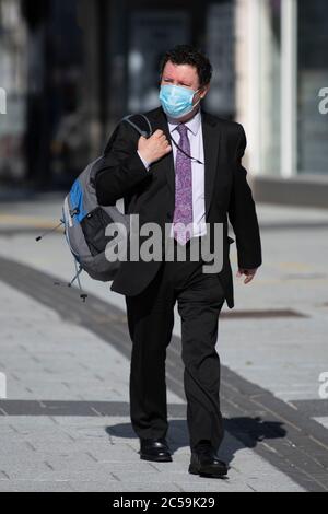 Un uomo d'affari che indossa un vestito e una maschera chirurgica cammina attraverso il centro di Cardiff durante il blocco del coronavirus a Cardiff, Galles, Regno Unito. Foto Stock