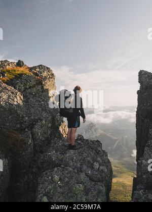 Giovane maschio con zaino si alza su una scogliera e inizia a paesaggio, Cantabria, Spagna Foto Stock