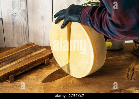 L'uomo taglia il formaggio con un coltello su un tavolo di legno Foto Stock