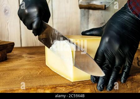 L'uomo taglia un pezzo di formaggio con un coltello un tavolo di legno Foto Stock