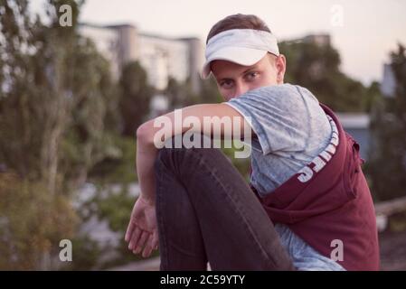 ritratto di un giovane ragazzo seduto sul tetto. Sullo sfondo del sole che tramonta. Concetto di solitudine Foto Stock