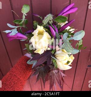Bouquet di bellissimi fiori e rami dall'inizio della primavera tenuto di fronte a una superficie viola Foto Stock
