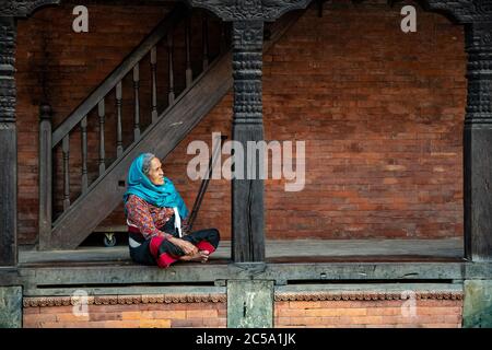 Anziana donna nepalese seduta sulla veranda della sua tipica casa in stile Newa a Bhaktapur, Nepal Foto Stock