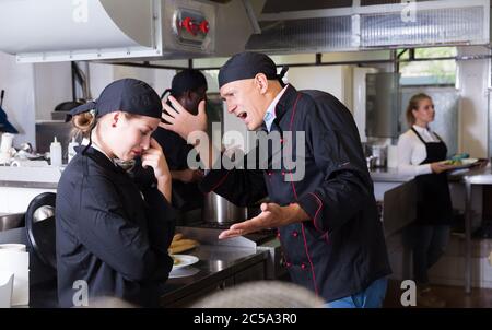 Arrabbiato chef maschio a parlare con il suo assistente femmina in cucina commerciale Foto Stock