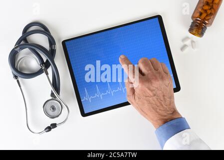Un cardiologo ha girato ad alto angolo, consegnando un tablet con un computer medico e un grafico EKG con flacone di pillola e stetoscopio. Foto Stock