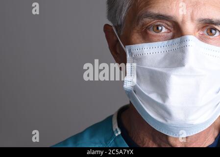 Ritratto di un medico maschile maturo che indossa una maschera chirurgica. Viene visualizzata solo una faccia parziale con lo spazio di copia su uno sfondo grigio. Foto Stock