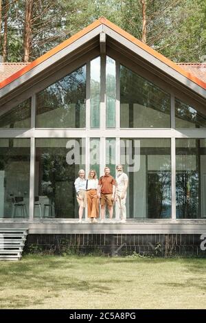 Ritratto di famiglia felice composto di bambini più grandi e genitori anziani in piedi contro bella casa con parete di vetro Foto Stock