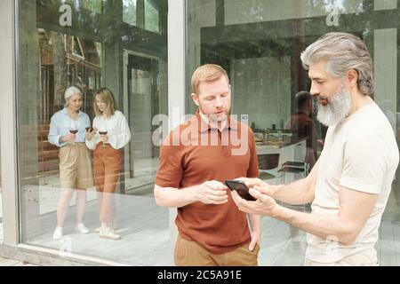 Uomo anziano che ha chiesto al figlio adulto di app per smartphone mentre parlano di tecnologia in casa Foto Stock