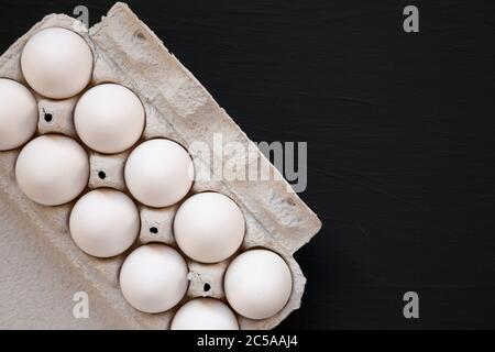 Uova bianche biologiche non cotte in una scatola di carta su una superficie nera, vista dall'alto. Spazio di copia. Foto Stock