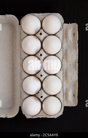 Uova bianche biologiche non cotte in una scatola di carta su una superficie nera, vista dall'alto. Posa piatta, sovratesta, dall'alto. Foto Stock