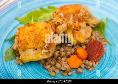 Cotto al forno cosce di pollo con orzo porridge servito con brasato di verdure fresche e foglie di rucola Foto Stock