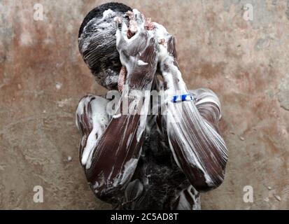 Ghana, Accra, Jamestown. Un giovane giocatore di calcio bagni in un bagno locale al villaggio di pescatori di Jamestown. Gioca per il Kindoku FC di Accra e sostiene Foto Stock