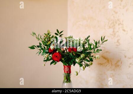 bouquet nuziale di rose rosse e rosa, rami di bosso, boccioli non fiorenti di fiori bianchi e nastri rossi con broccia nel vaso di vetro Foto Stock