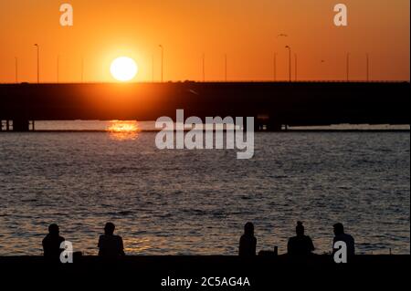 Helsinki / Finlandia - 26 GIUGNO 2020: Sagome di persone felici che godono il tempo estivo a riva durante il tramonto. Foto Stock