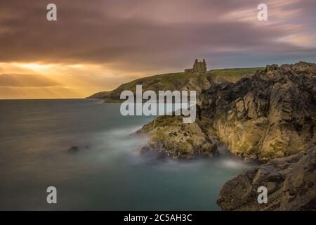 Lunga esposizione della costa scozzese con il castello di Dunskey sullo sfondo e raggi di sole sulle scogliere. Foto Stock