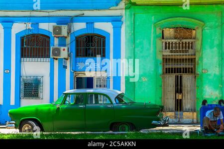 Havana, Cuba, 2019 luglio, vista di una vecchia auto americana parcheggiata di fronte a due edifici colorati in Calle San Juan de Dios, nella parte vecchia della città Foto Stock