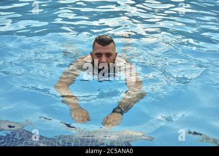 Uomo bearded che nuota in una piscina. Uomo con barba in piscina. Foto Stock